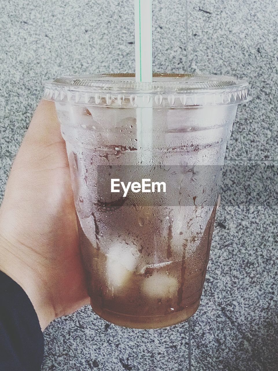 Close-up of hand holding cold drink in disposable cup by wall