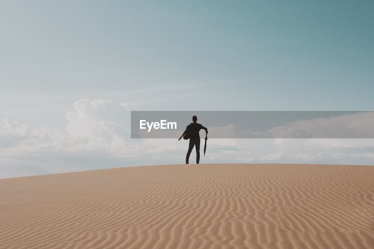 Rear view of man holding umbrella on desert against sky