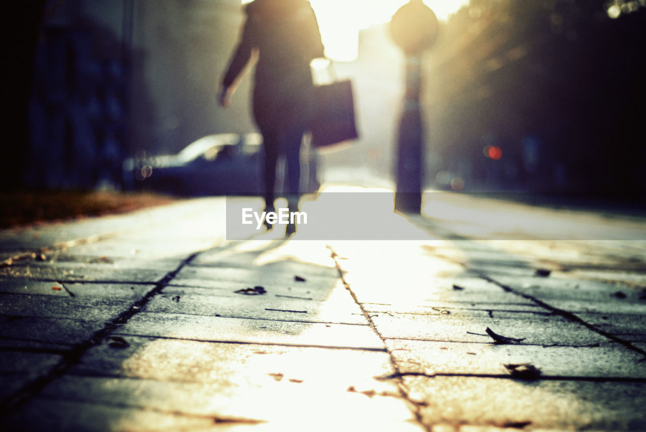 Low section of silhouette woman walking on street