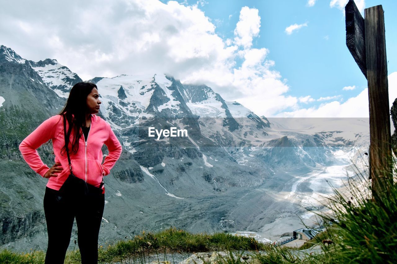 Young woman standing on snowcapped mountain against sky