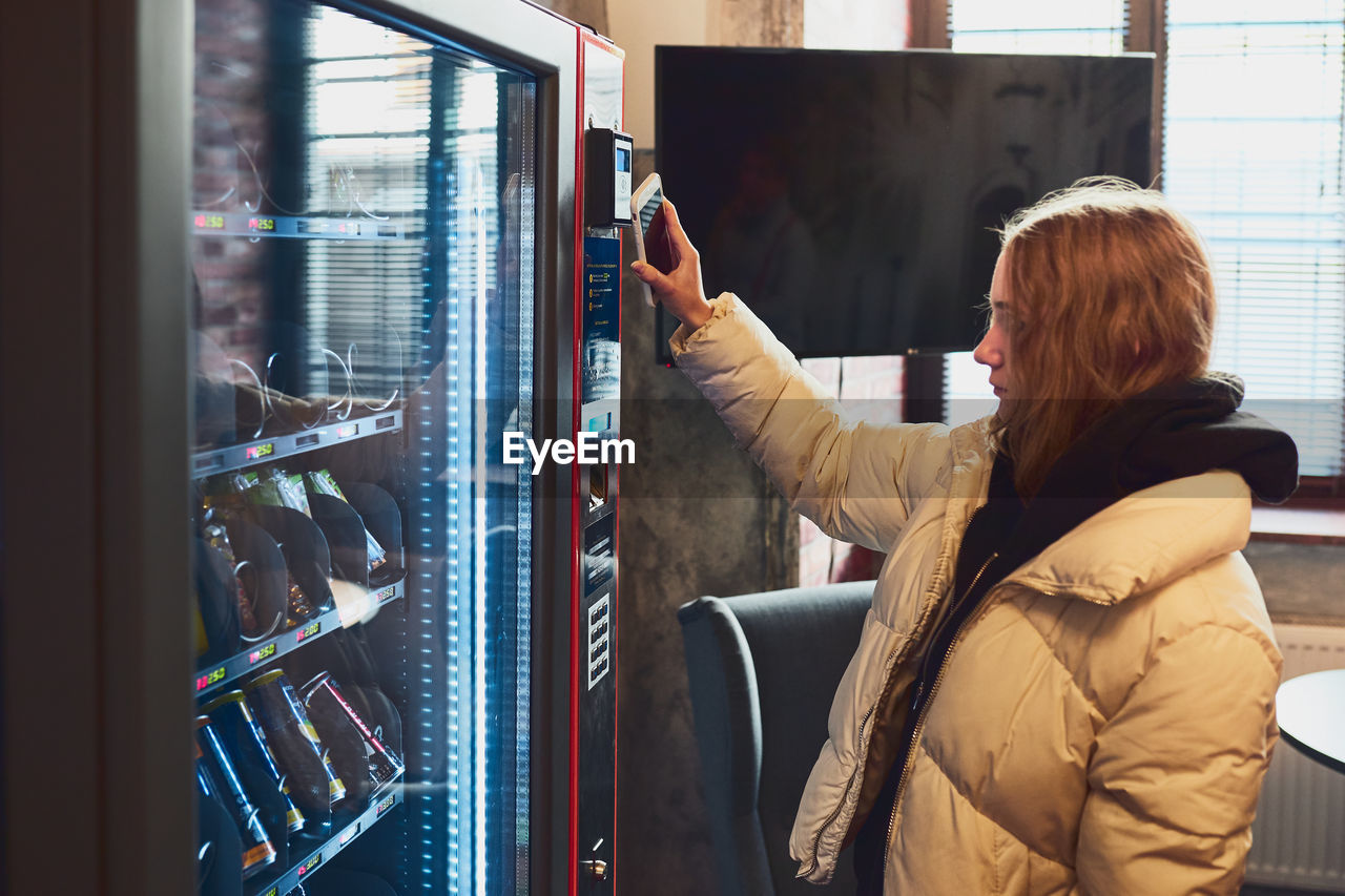 Woman paying for product at vending machine using contactless method of payment with mobile phone