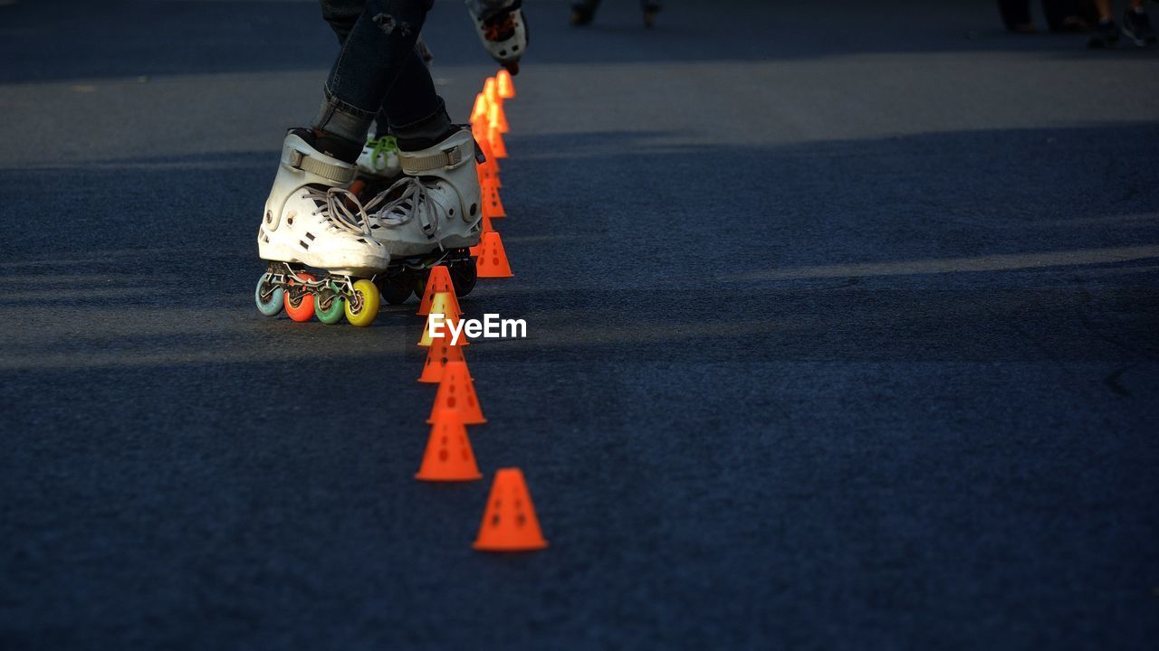 Low section of person roller skating by traffic cones on road