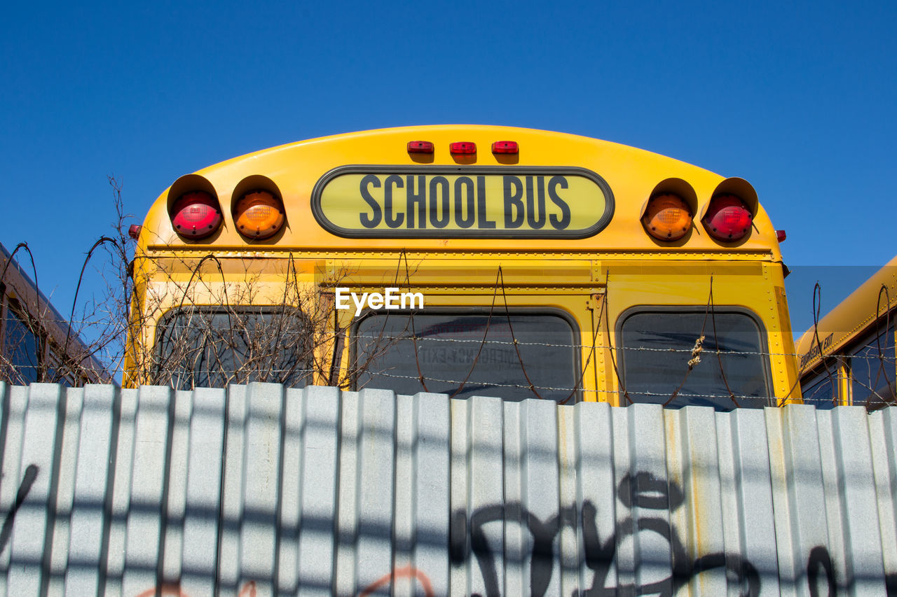 School bus by corrugated iron against clear blue sky