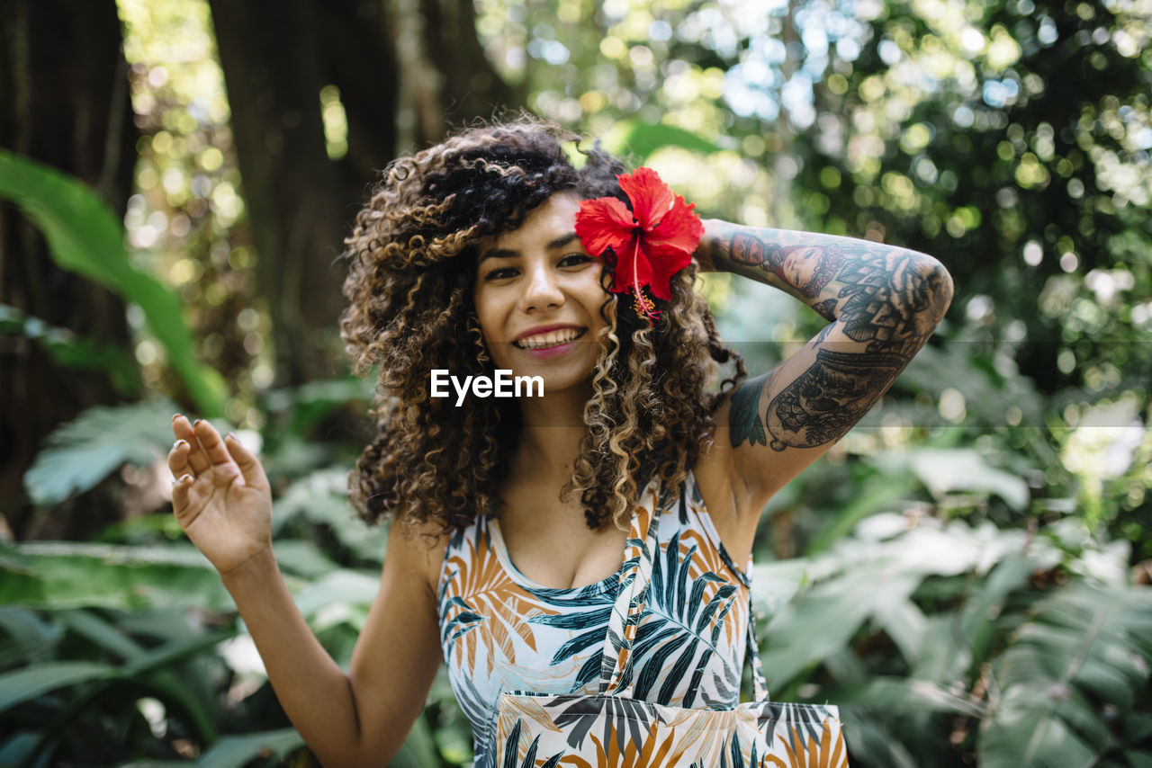 Portrait of smiling young woman standing against plants in forest