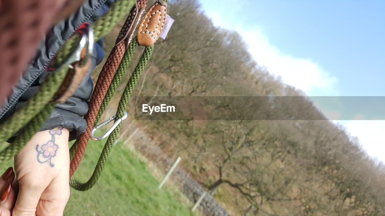 Low angle view of cropped hand with climbing rope against trees