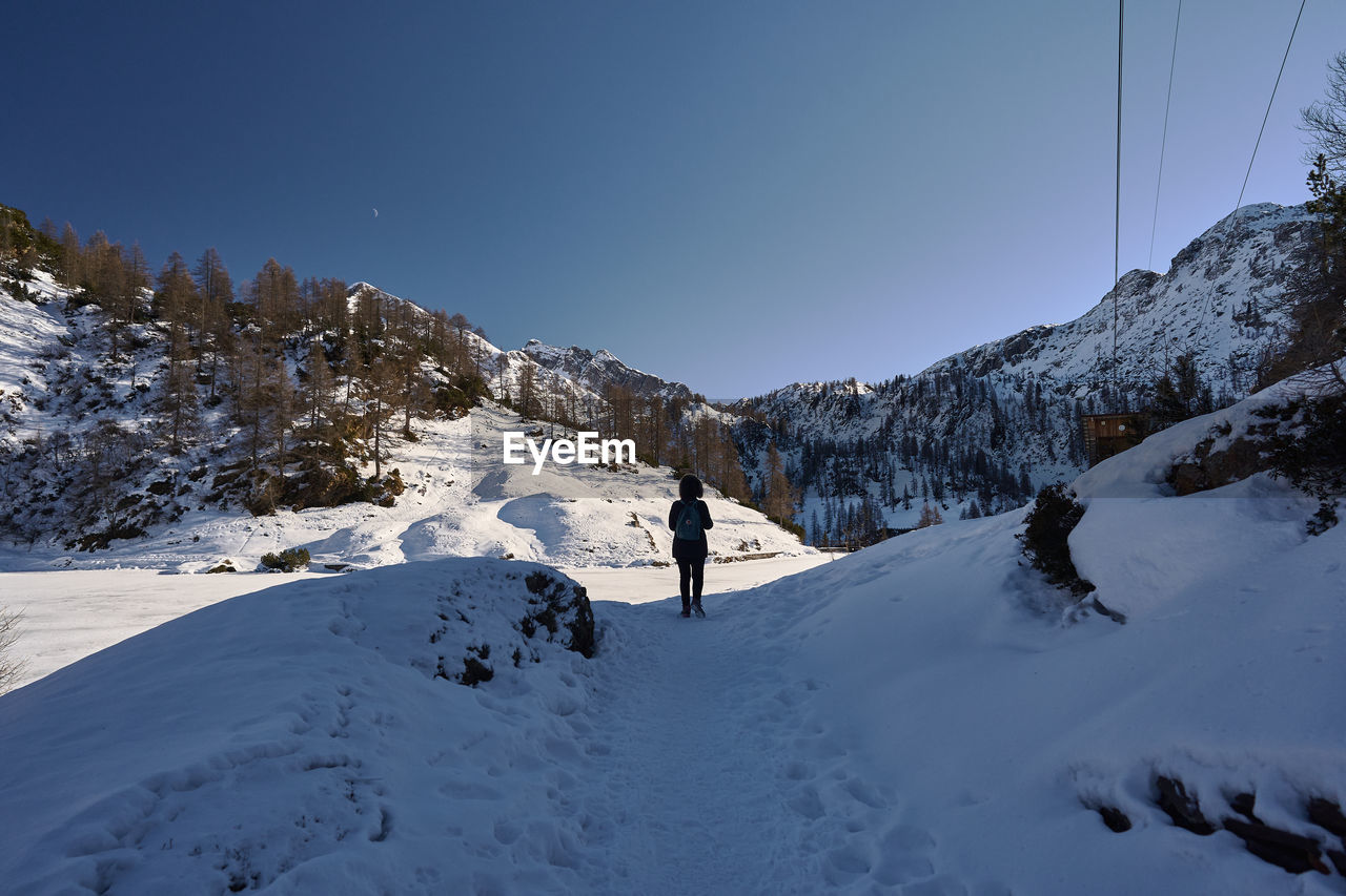 snow, winter, cold temperature, mountain, scenics - nature, sky, environment, mountain range, sports, skiing, nature, landscape, beauty in nature, adventure, winter sports, snowcapped mountain, leisure activity, footwear, travel, ski mountaineering, ski touring, tree, one person, travel destinations, land, vacation, coniferous tree, forest, holiday, trip, pinaceae, piste, ski equipment, ski, outdoors, full length, activity, blue, climbing, day, clear sky, extreme sports, pine tree, ski holiday, non-urban scene, mountain climbing, plant, adult, frozen, ridge, tourism, pine woodland