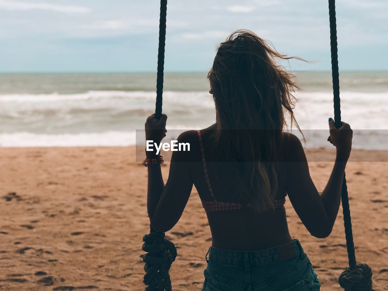 Rear view of woman sitting on swing at beach