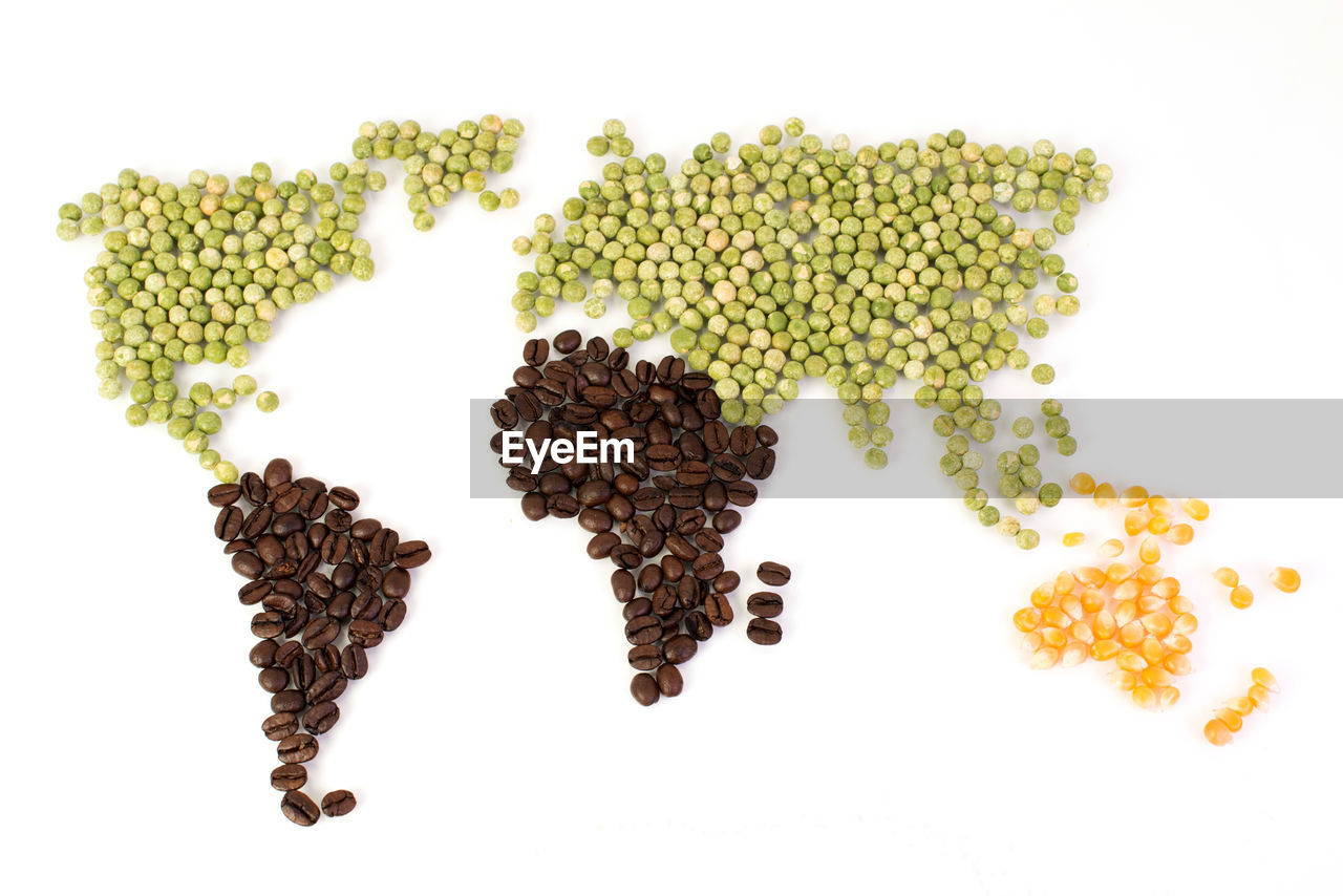 Green peas and roasted coffee beans in world map shape on white background