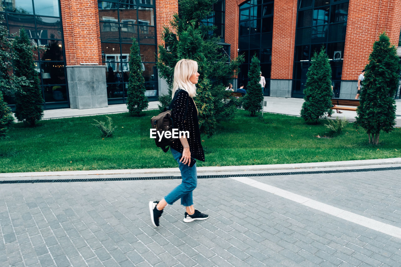 REAR VIEW OF WOMAN WALKING ON STREET AGAINST BUILDINGS