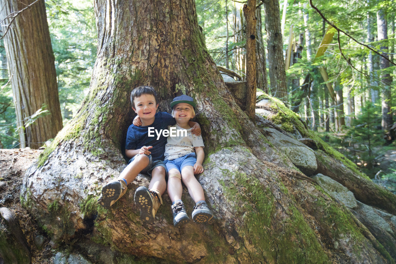Portrait of two friends sitting in root nook for old growth tree.