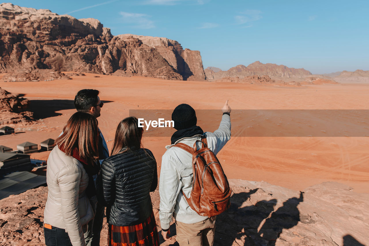 Back view of group of traveling friends standing in sandstone valley wadi rum and observing amazing landscape