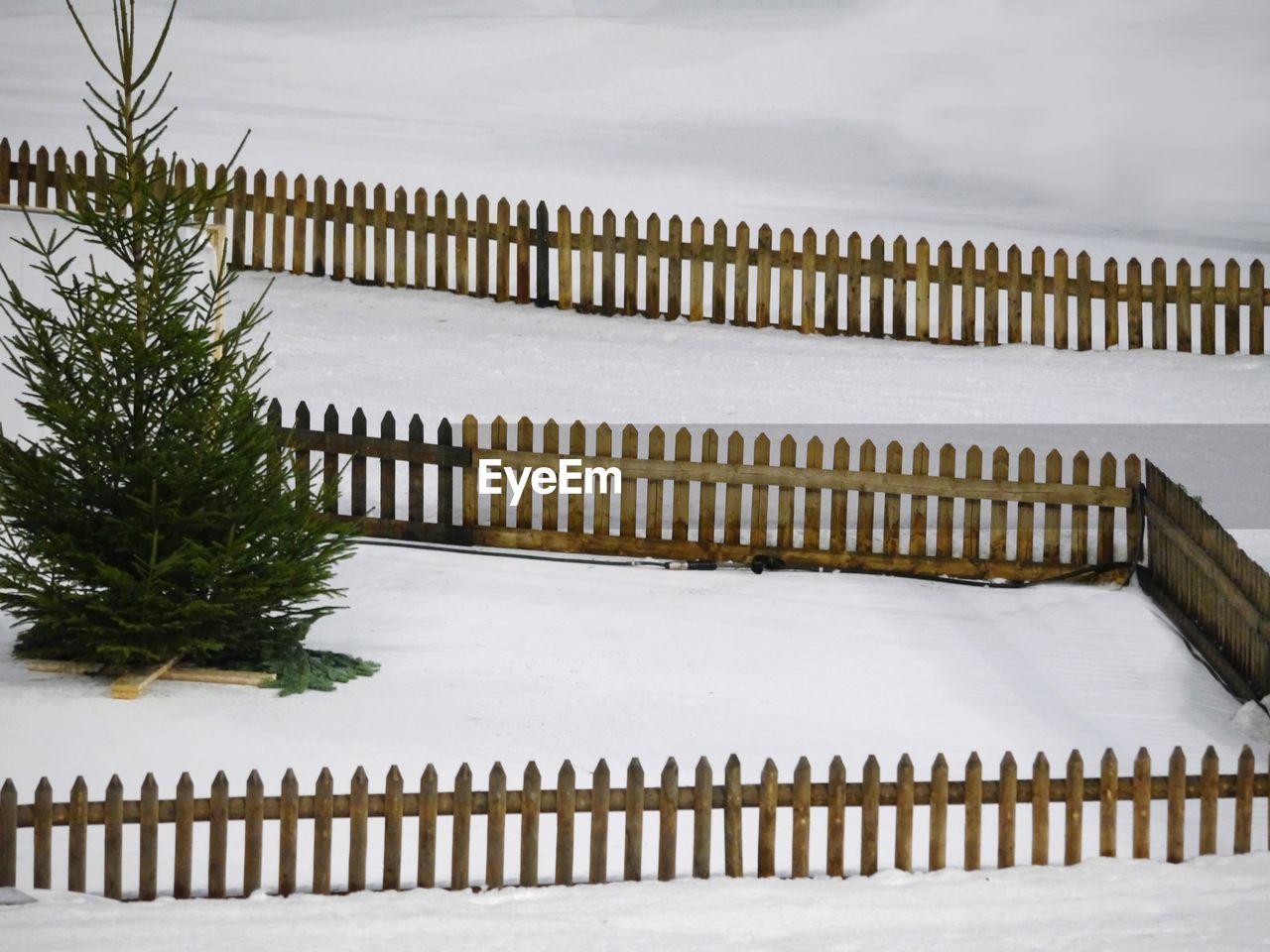 Wooden fence on snow covered field against sky