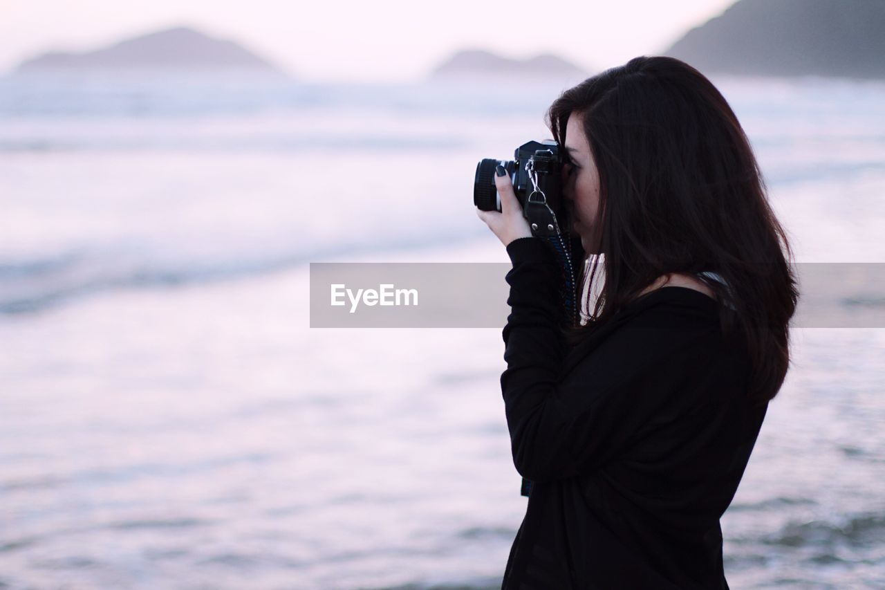 Side view of woman photographing from slr camera against sea