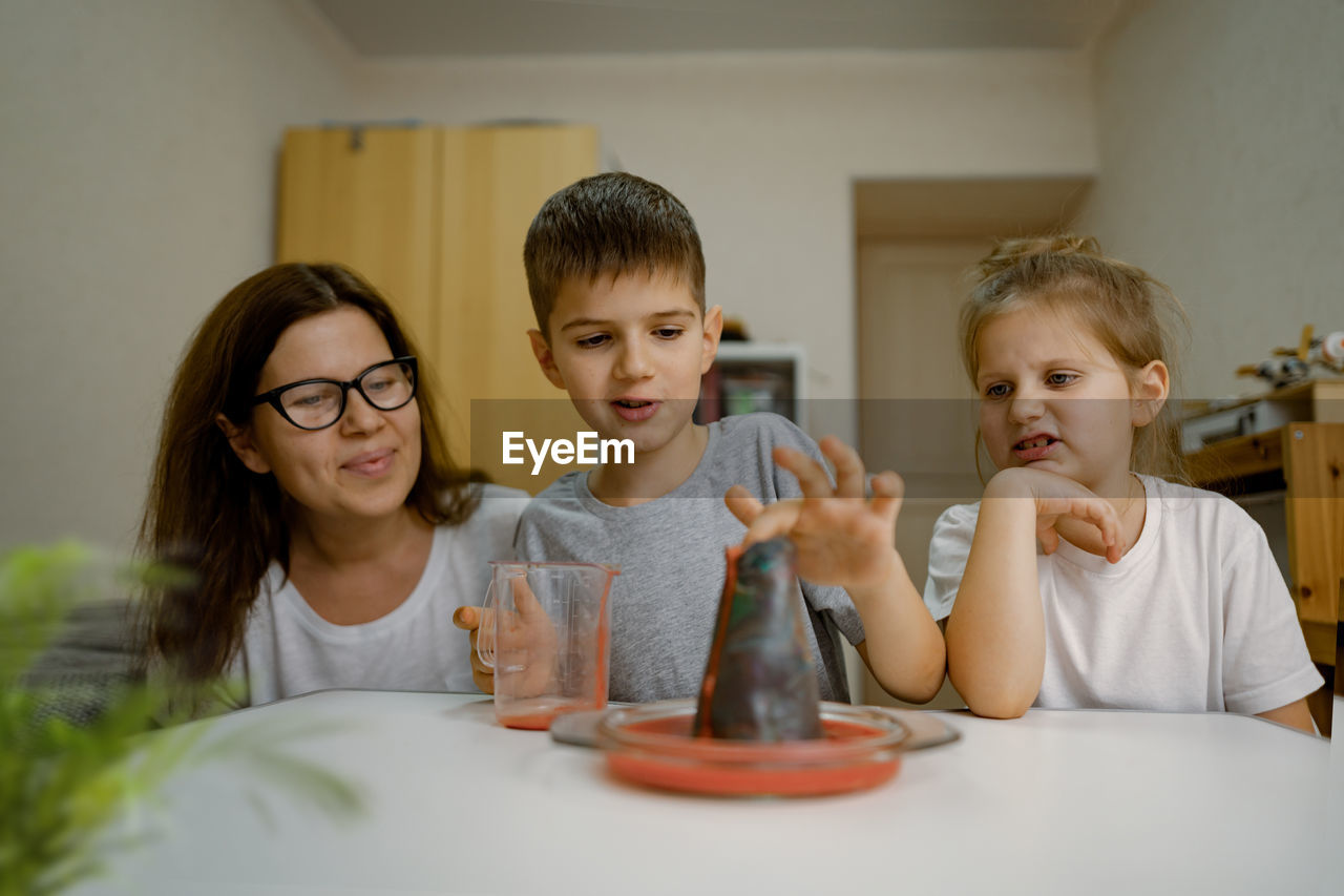 Mom and children at home are conducting an experiment with volcanic eruption.