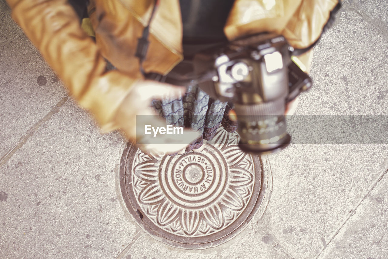 Low section of woman with camera standing on manhole