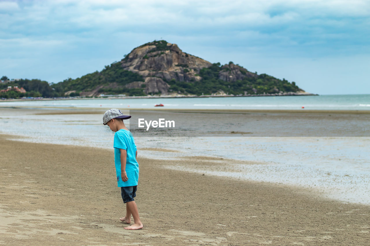 Boy playing on sand at beach against sky