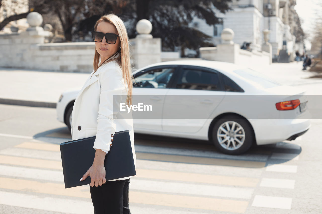 Woman wearing sunglasses standing against car in city