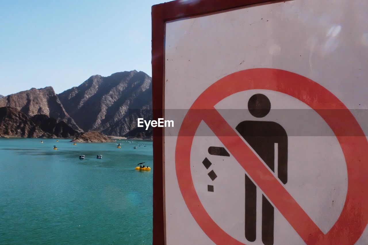 ROAD SIGN BY SEA AGAINST MOUNTAINS