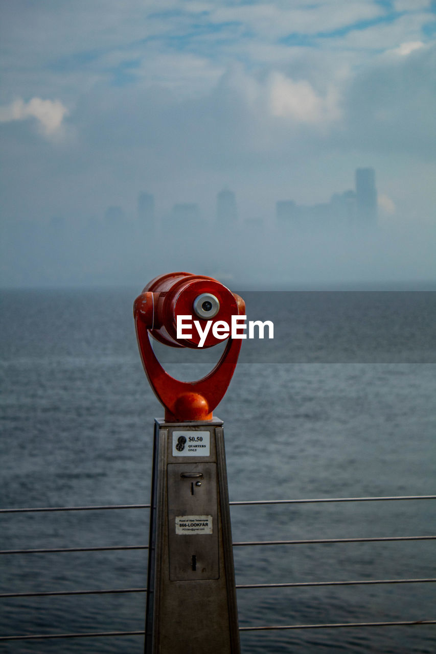 Coin operated telescope by sea against sky