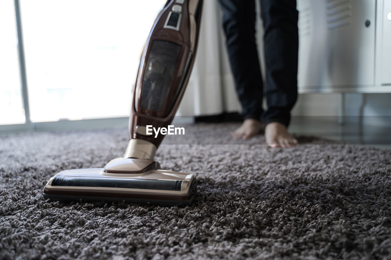 Low section of person cleaning rug with vacuum cleaner at home