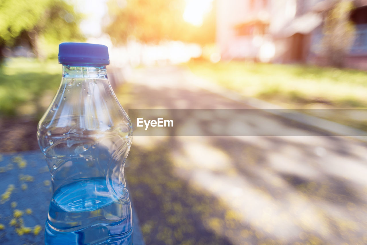 CLOSE-UP OF WATER BOTTLE AGAINST BLUE ROAD