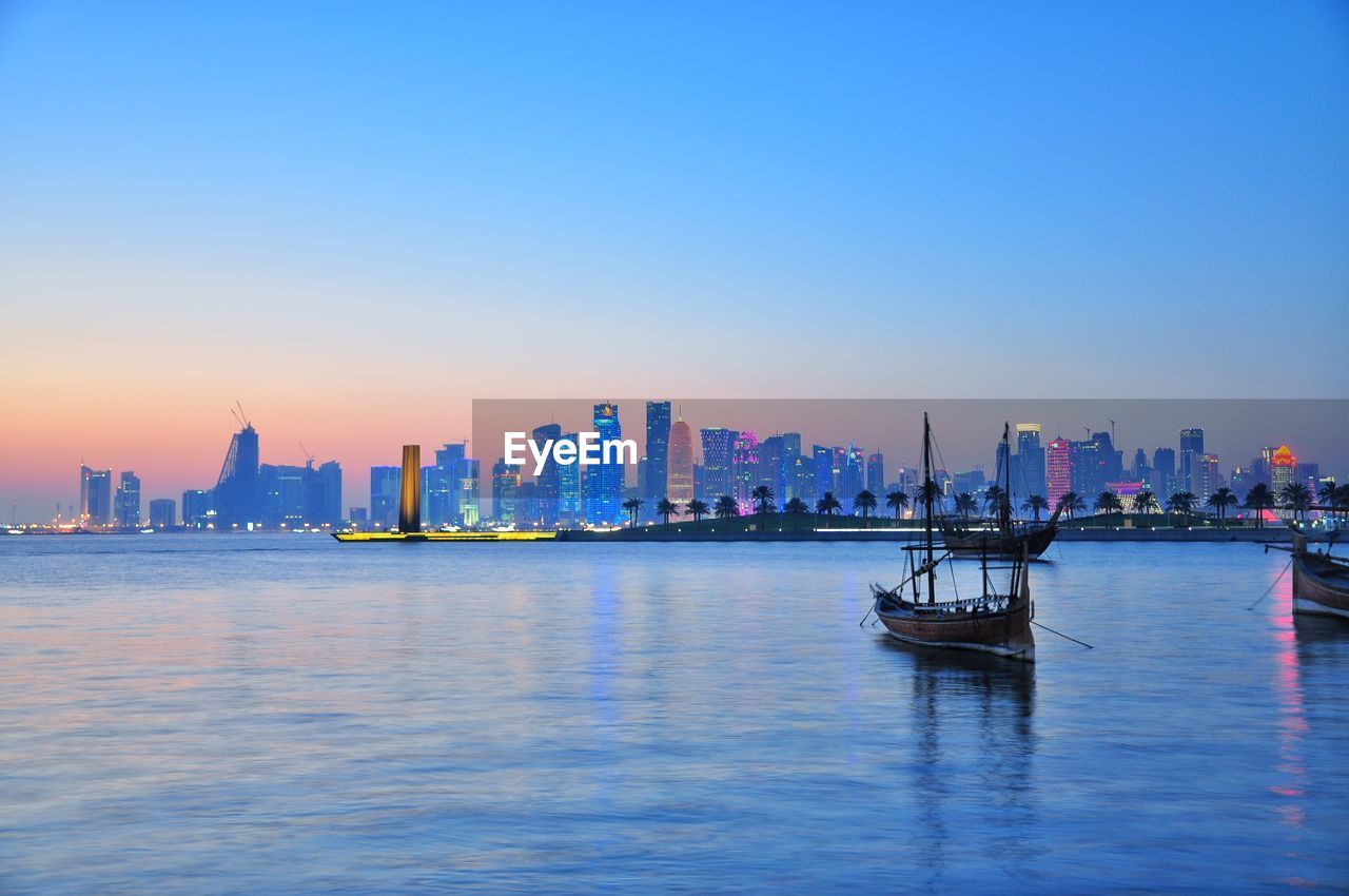 Boats on sea against modern buildings at sunset