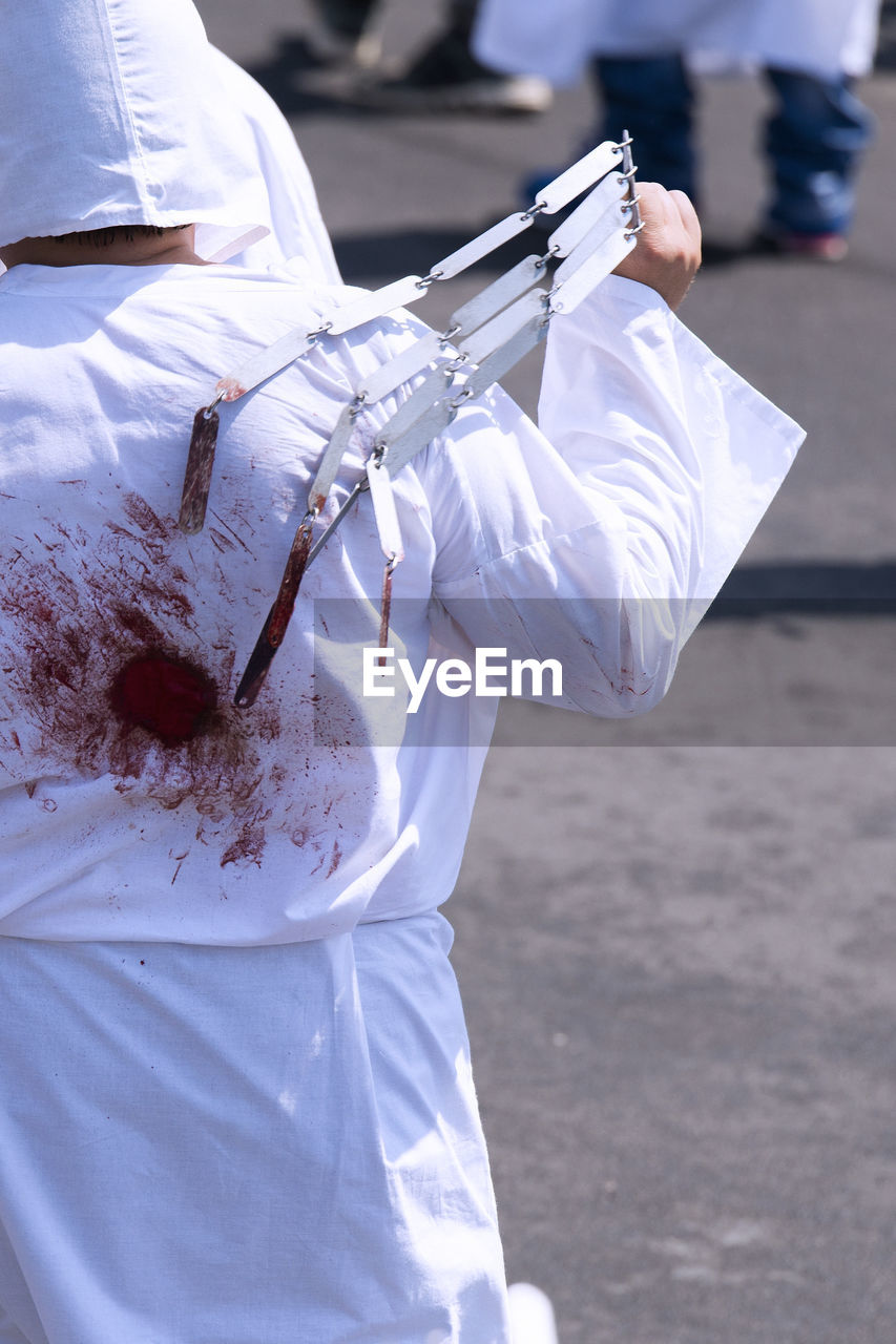 Rear view of man with injured body holding equipment during religious event