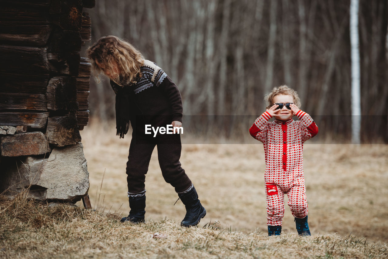 Kids walking in forest by wooden house wearing scandinavian onesies