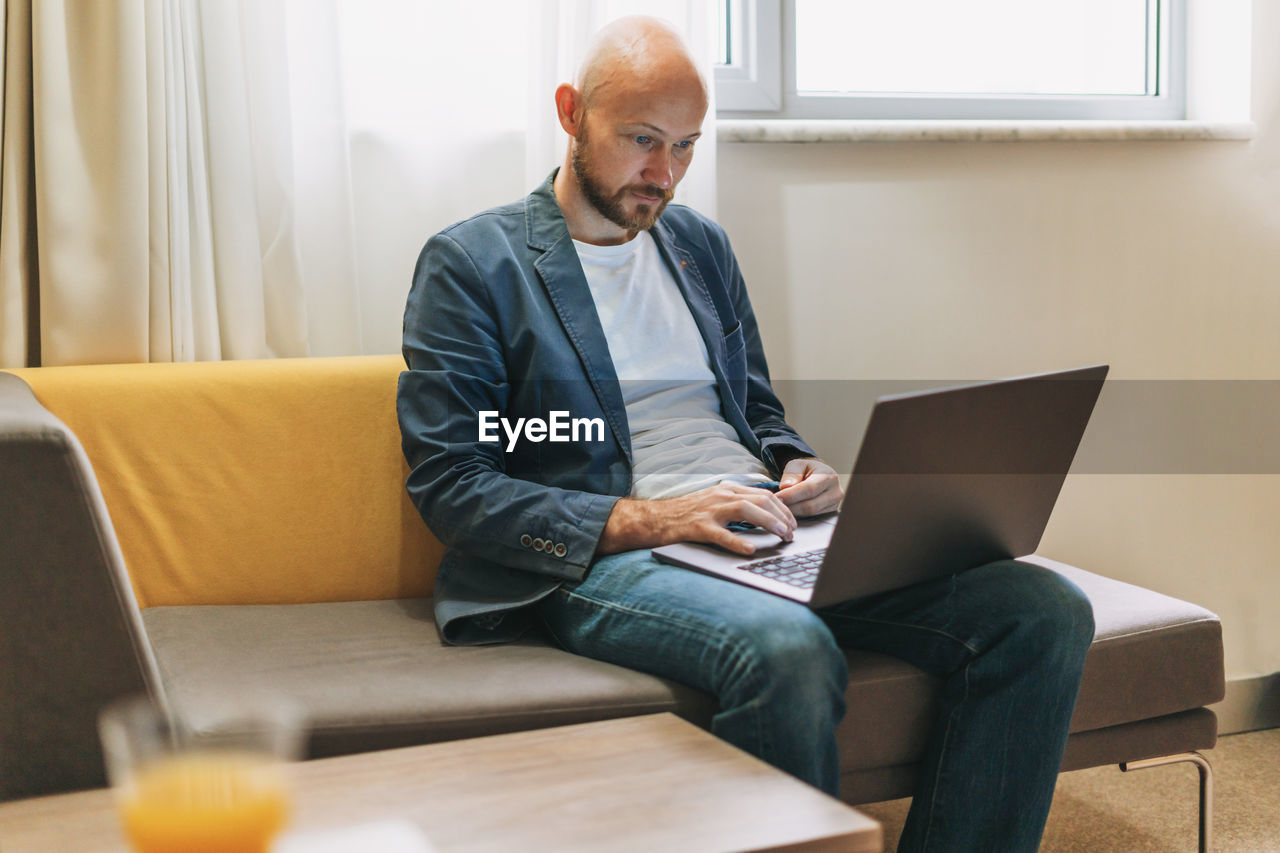 Smiling businessman using laptop sitting on sofa at home