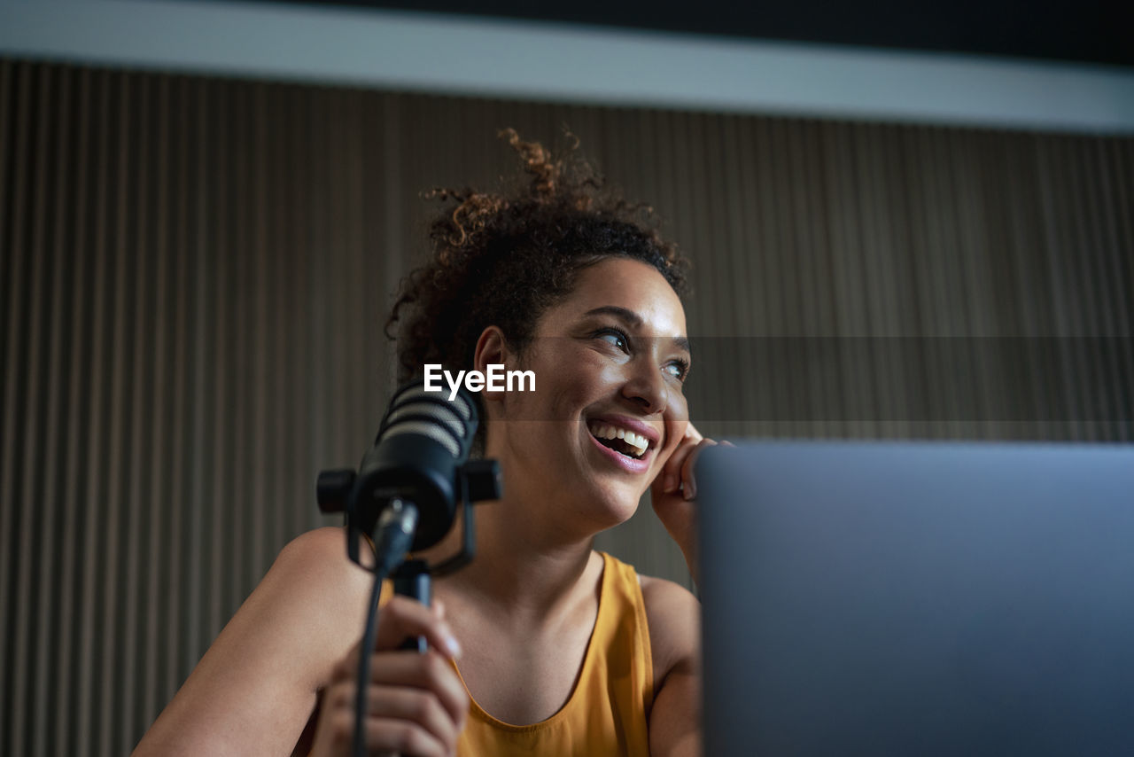 Happy radio presenter with microphone podcasting at workplace