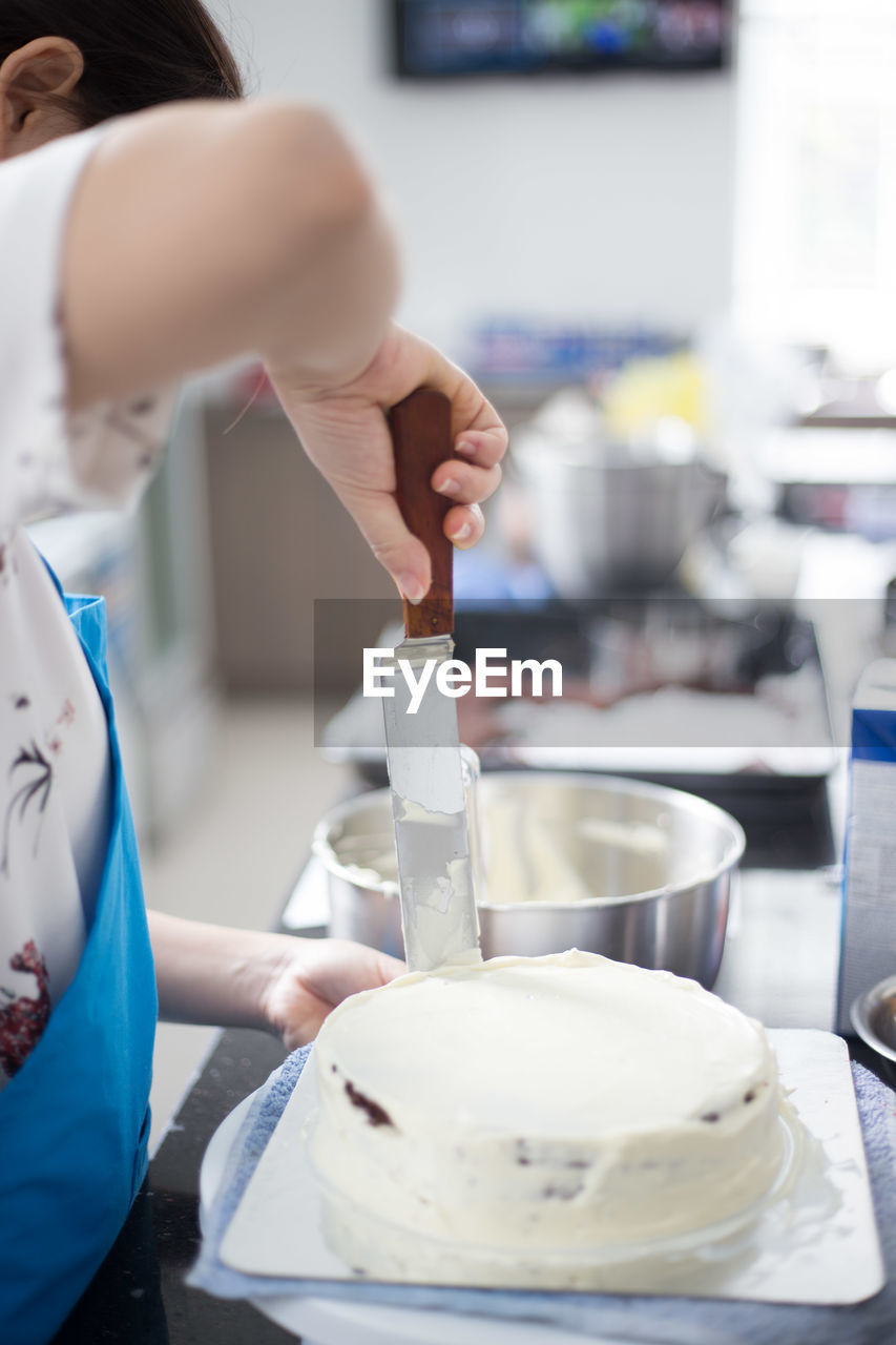 Cropped image of woman spreading cream on sponge cake at kitchen
