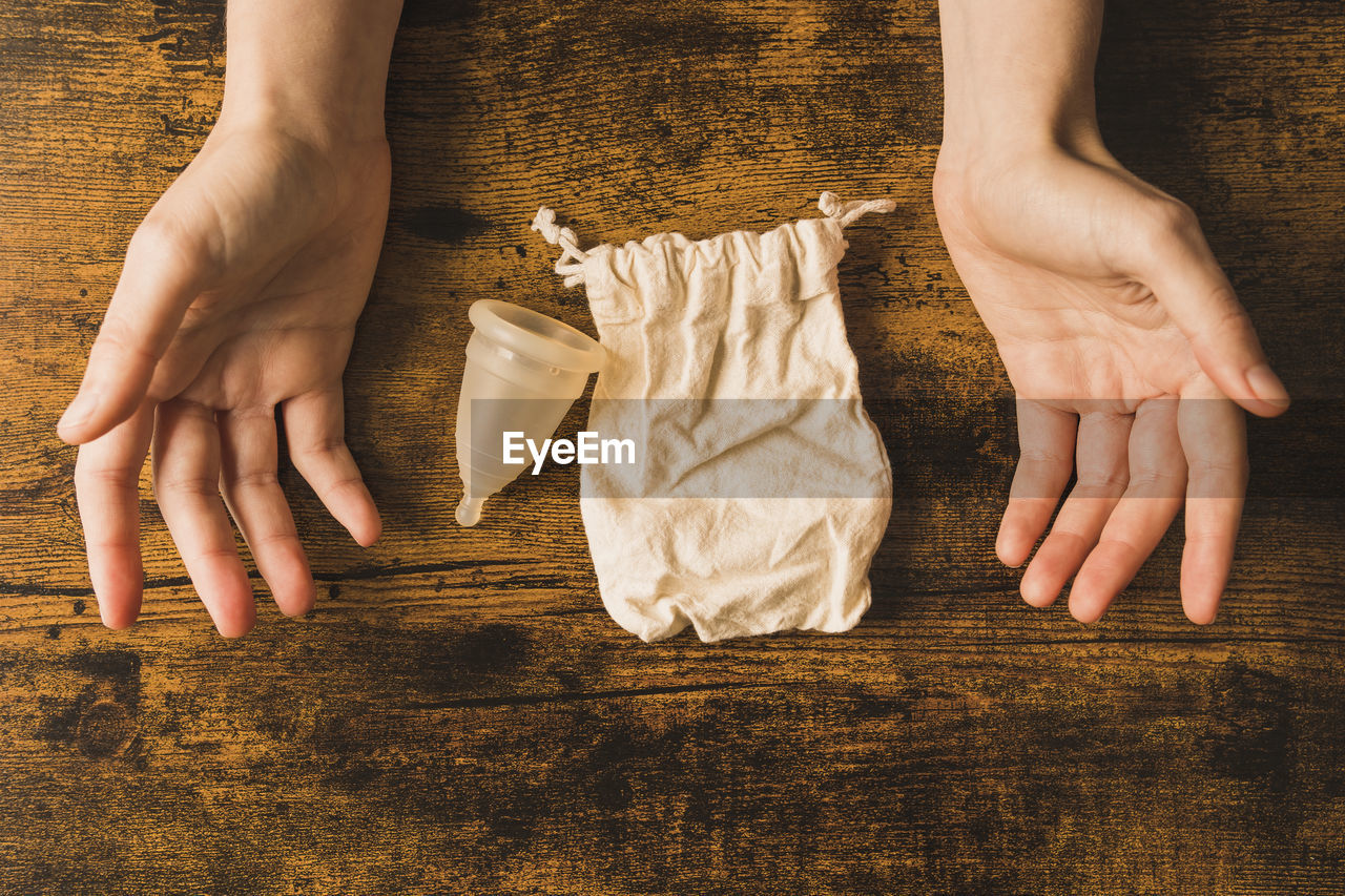 Woman with menstrual cup and cloth bag on wooden table