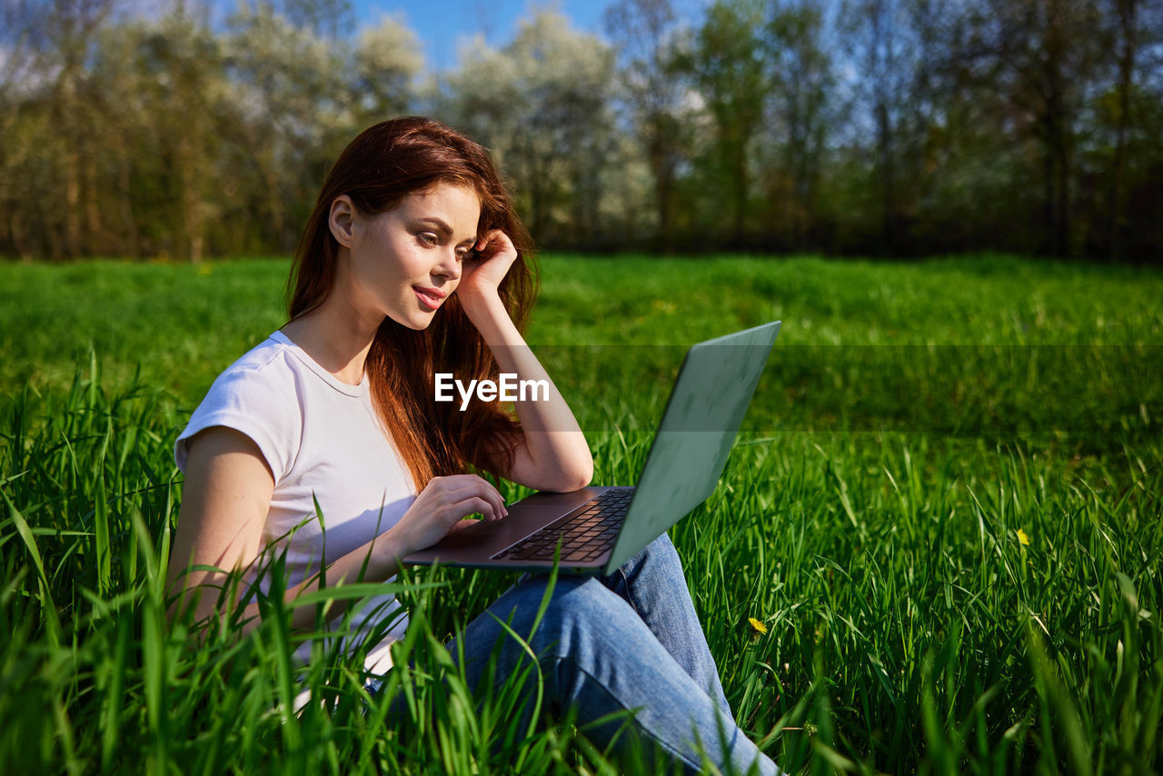 young woman using digital tablet while sitting on field