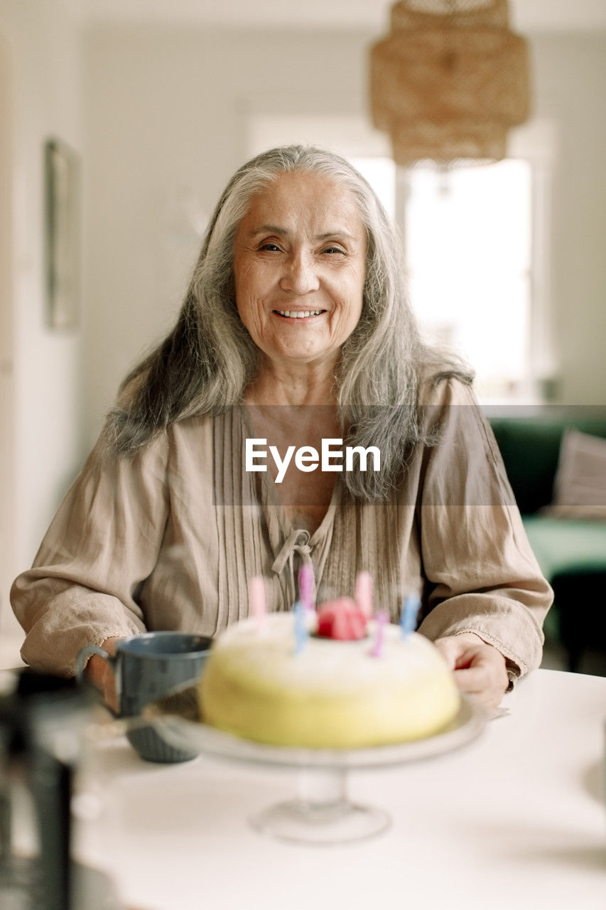 Portrait of smiling senior woman with birthday cake on table at home