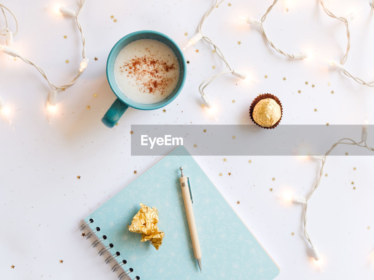 Close-up of coffee cup and chocolate with illuminated string lights on marble