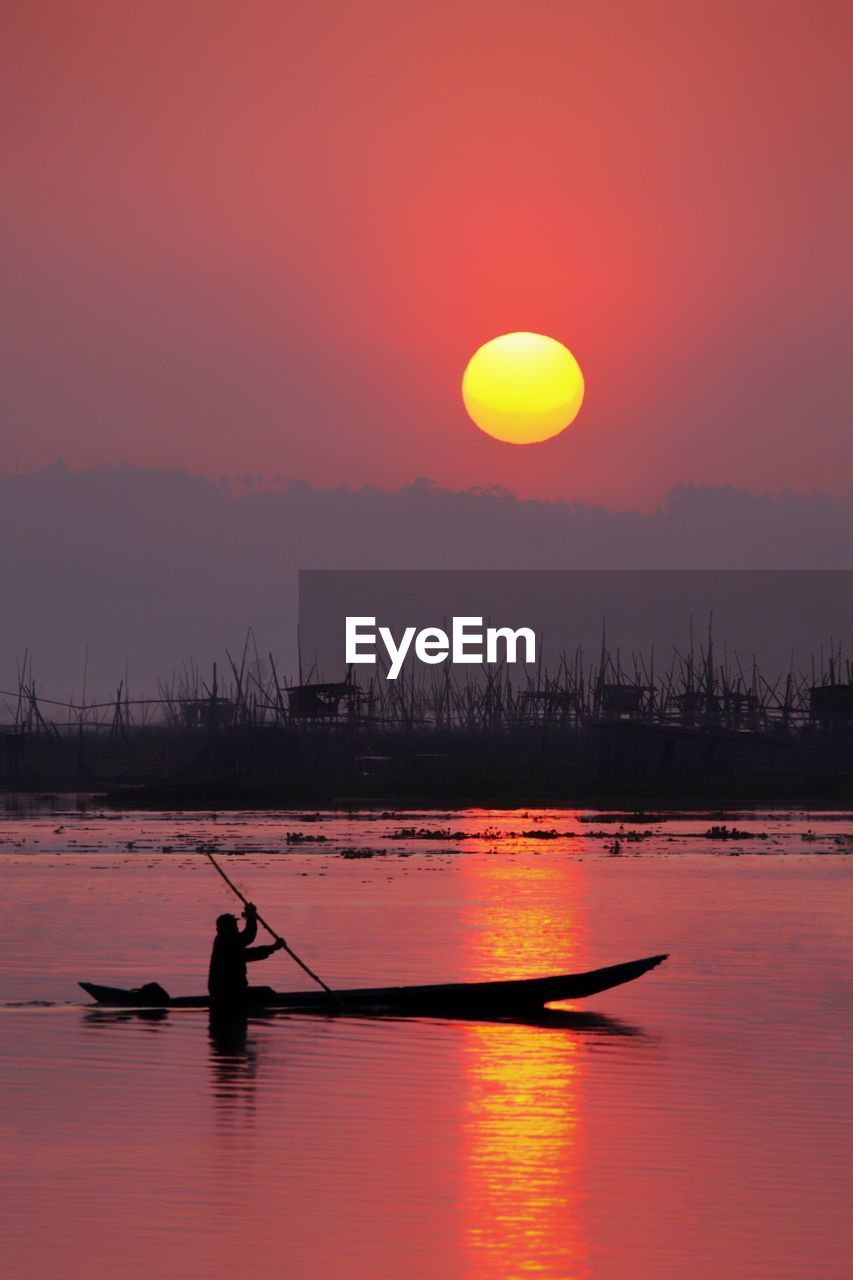 SILHOUETTE MAN ON BOAT AGAINST ORANGE SKY