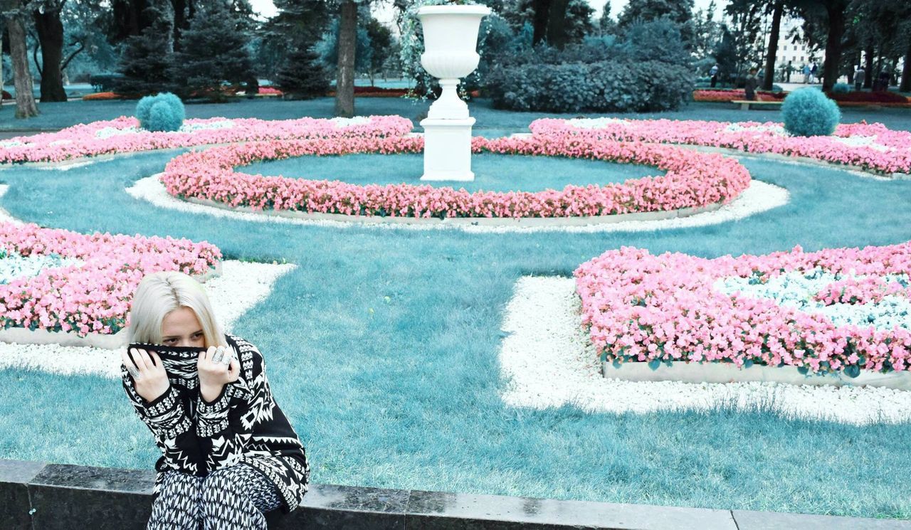 Woman looking away while sitting on retaining wall at park