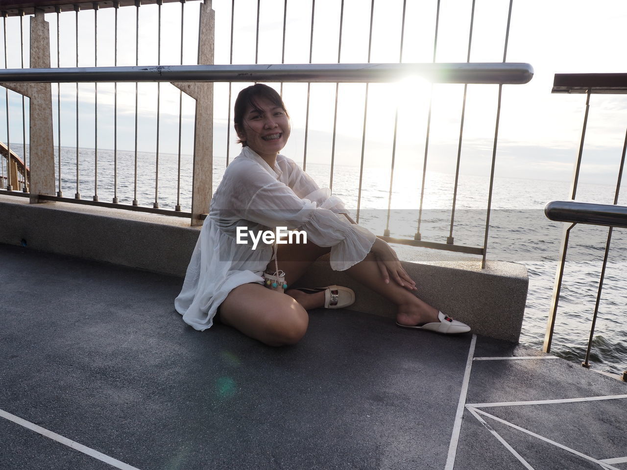 PORTRAIT OF A SMILING YOUNG WOMAN SITTING ON FLOOR IN WINDOW