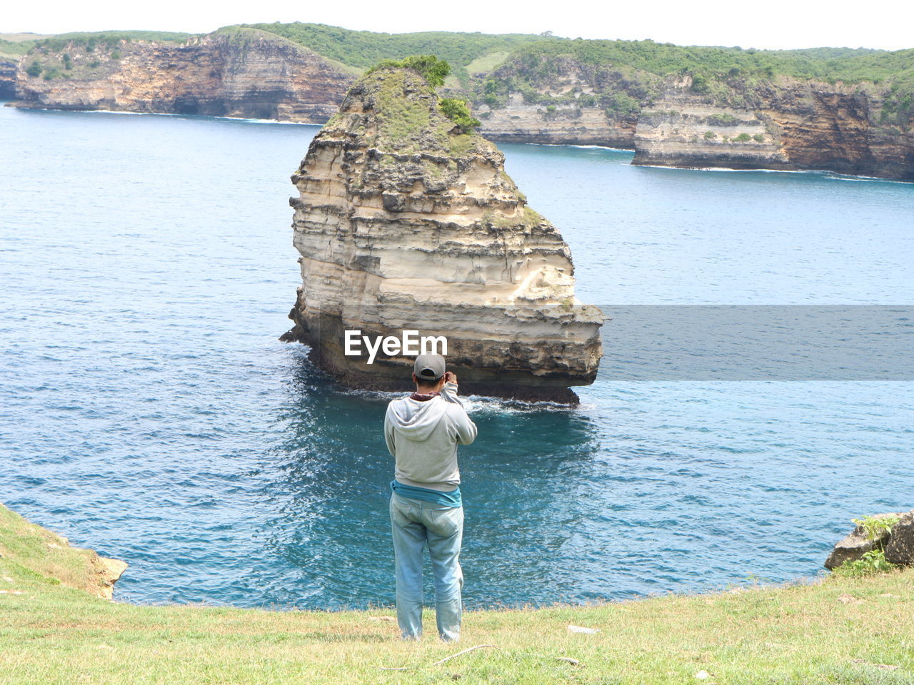 MAN STANDING ON ROCK AT SEA SHORE