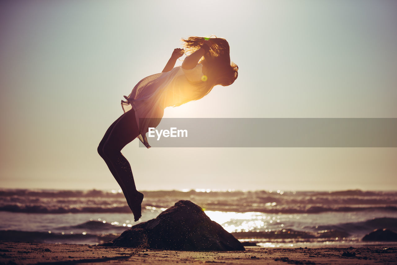 Full length side view of woman jumping on beach