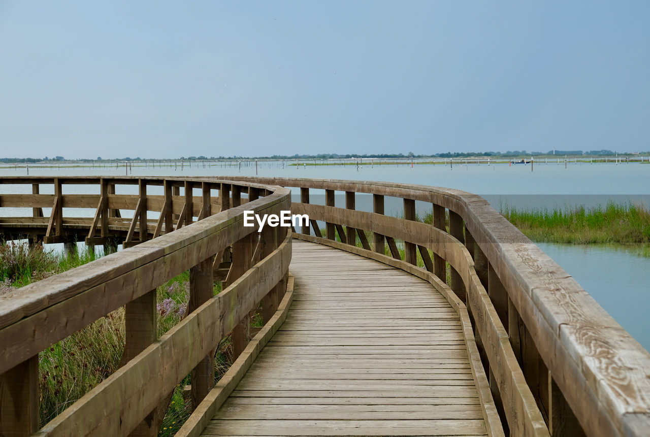 Wooden footbridge over sea against clear sky