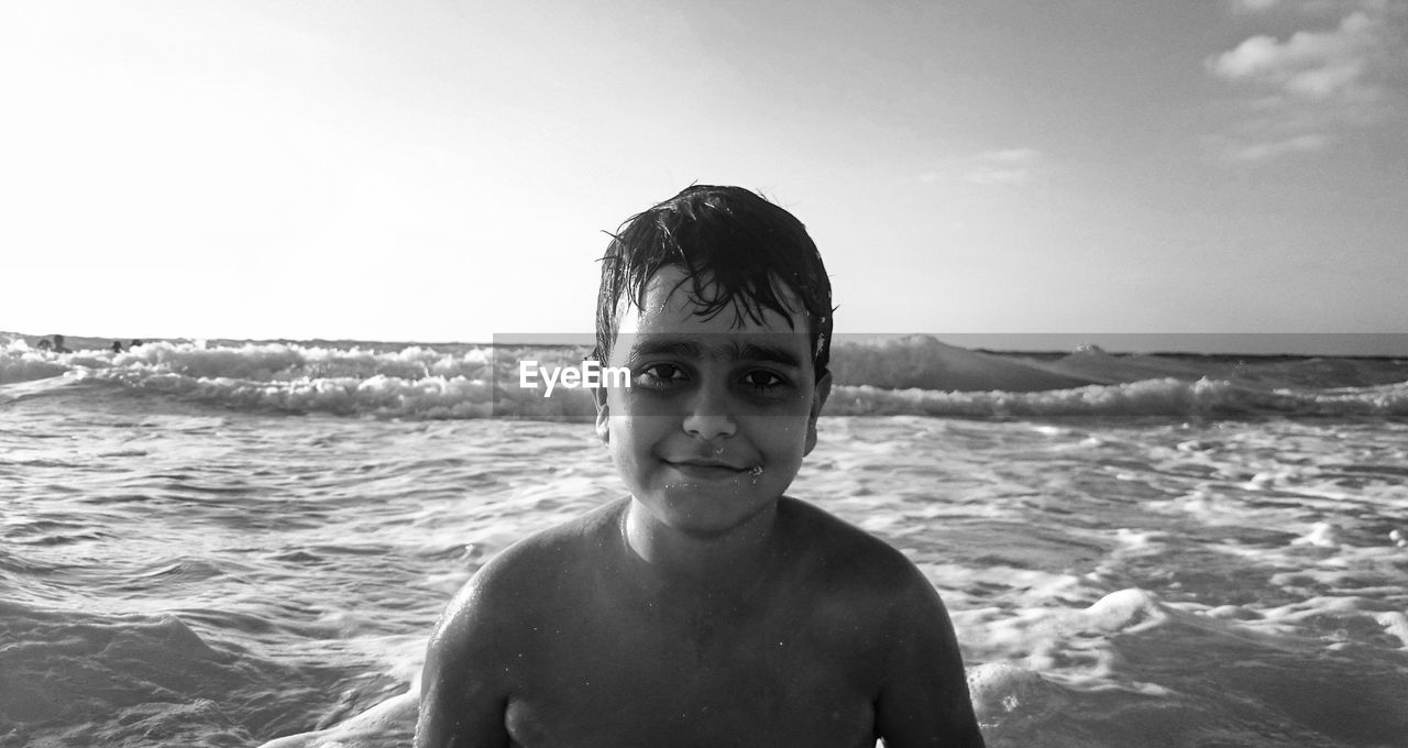 Close-up portrait of shirtless boy in sea against sky