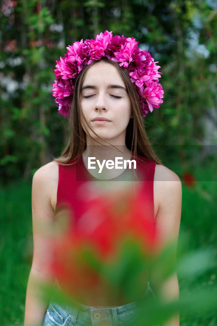 PORTRAIT OF BEAUTIFUL YOUNG WOMAN STANDING AGAINST PINK FLOWER