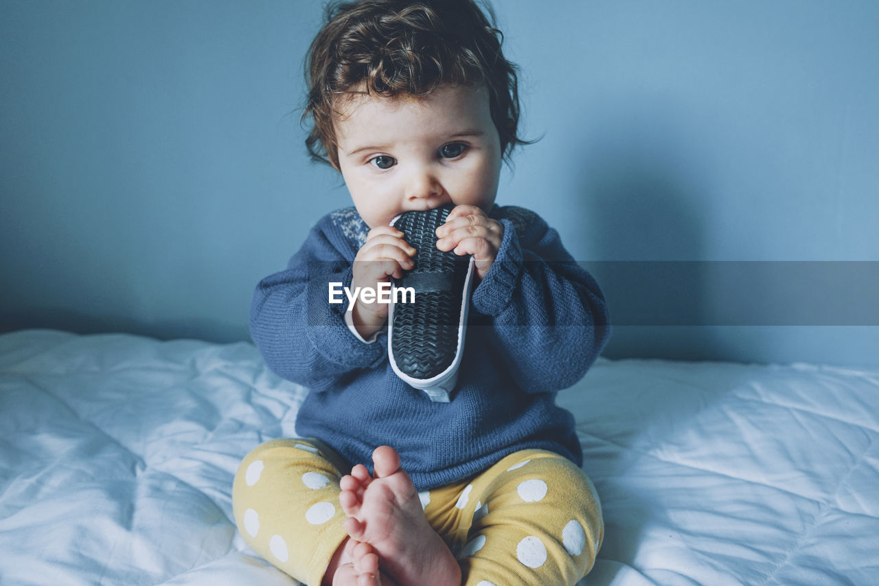 Cute girl biting shoe while sitting on bed at home