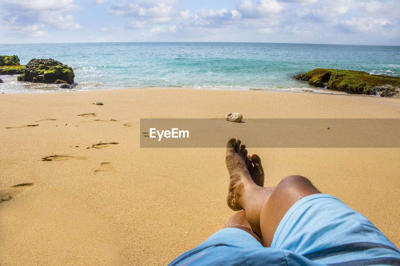 Low section of man relaxing on sand at beach