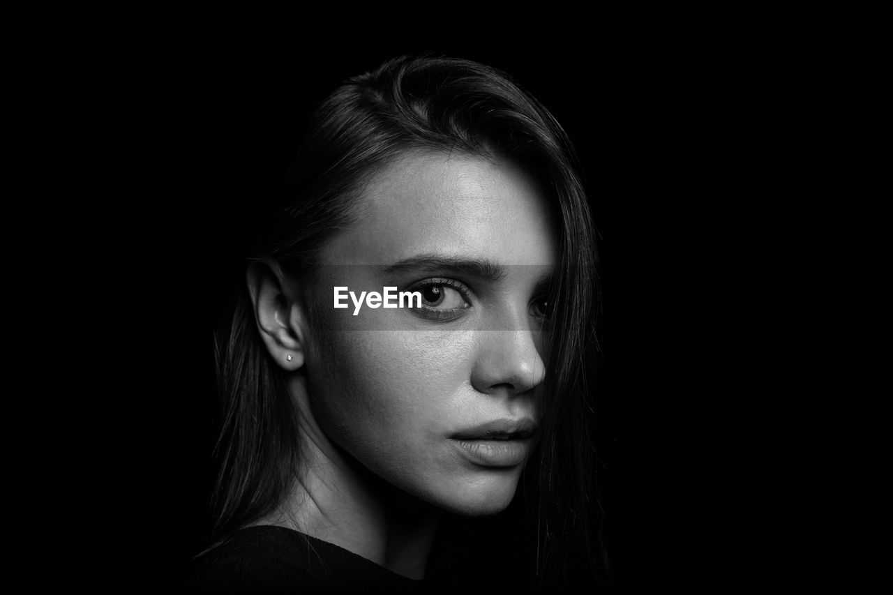 Close-up portrait of young woman over black background