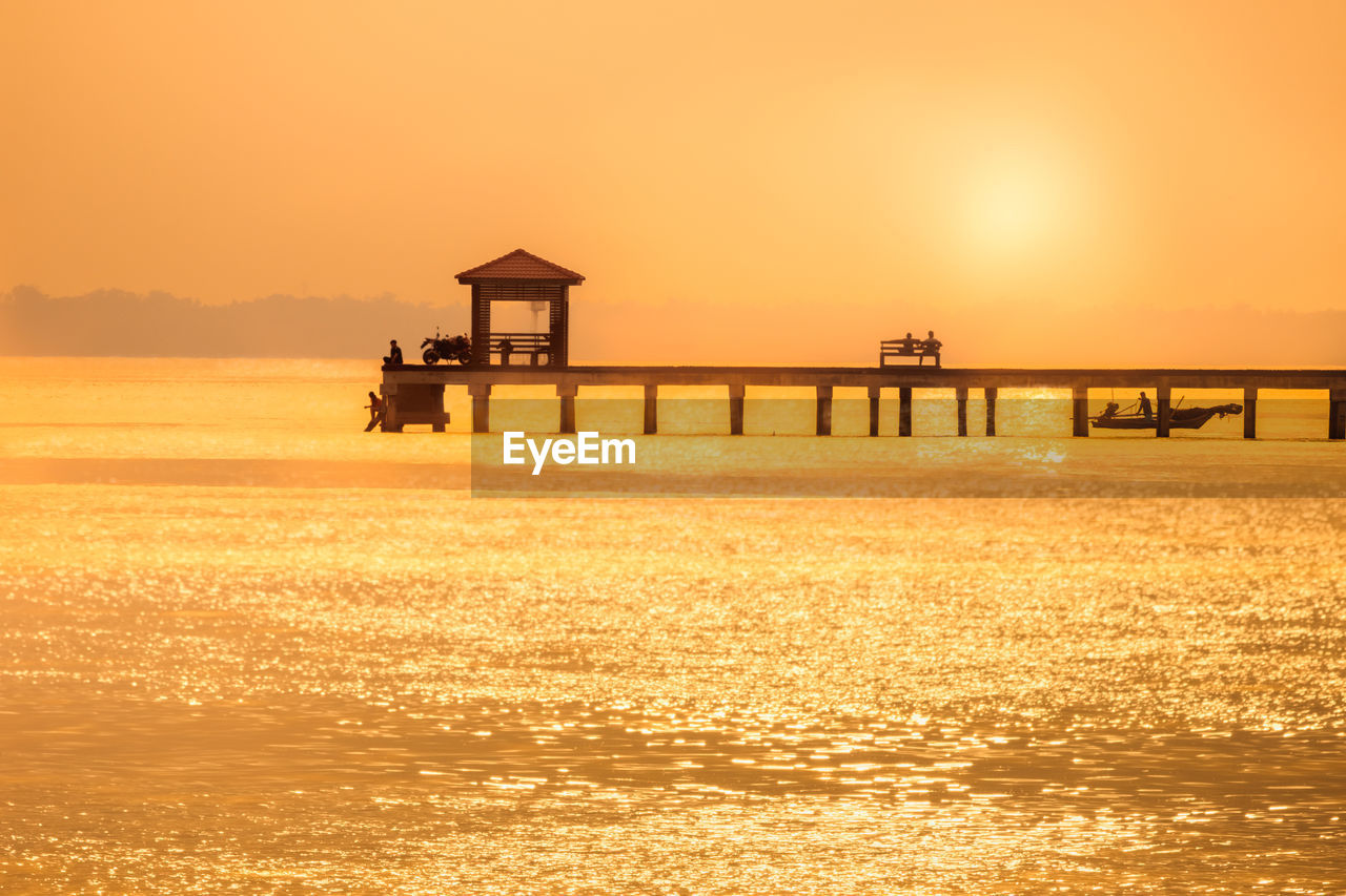 SILHOUETTE BUILT STRUCTURE ON SEA AGAINST SKY AT SUNSET