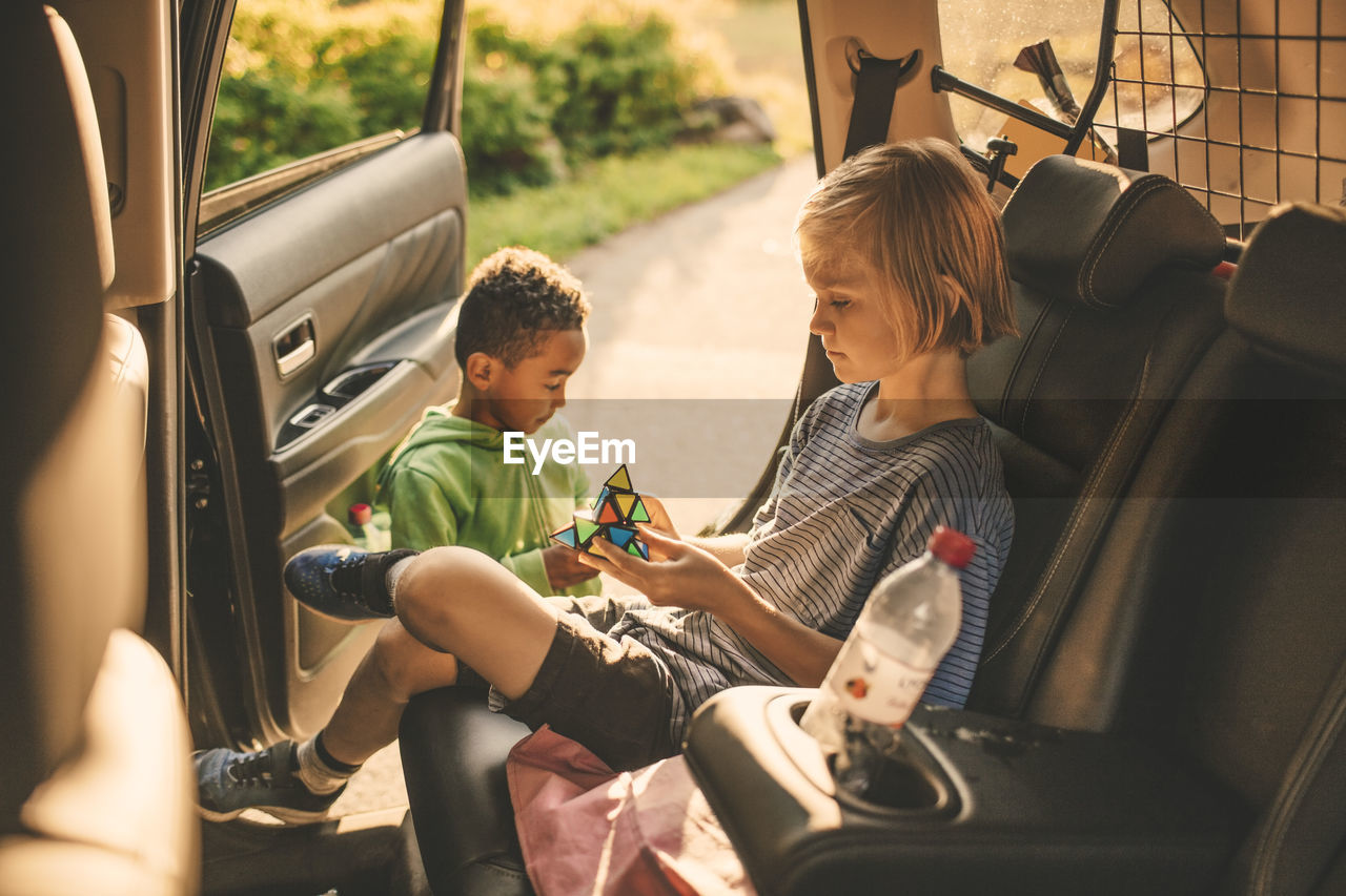 Girl playing puzzle cube while sitting in car by brother at park