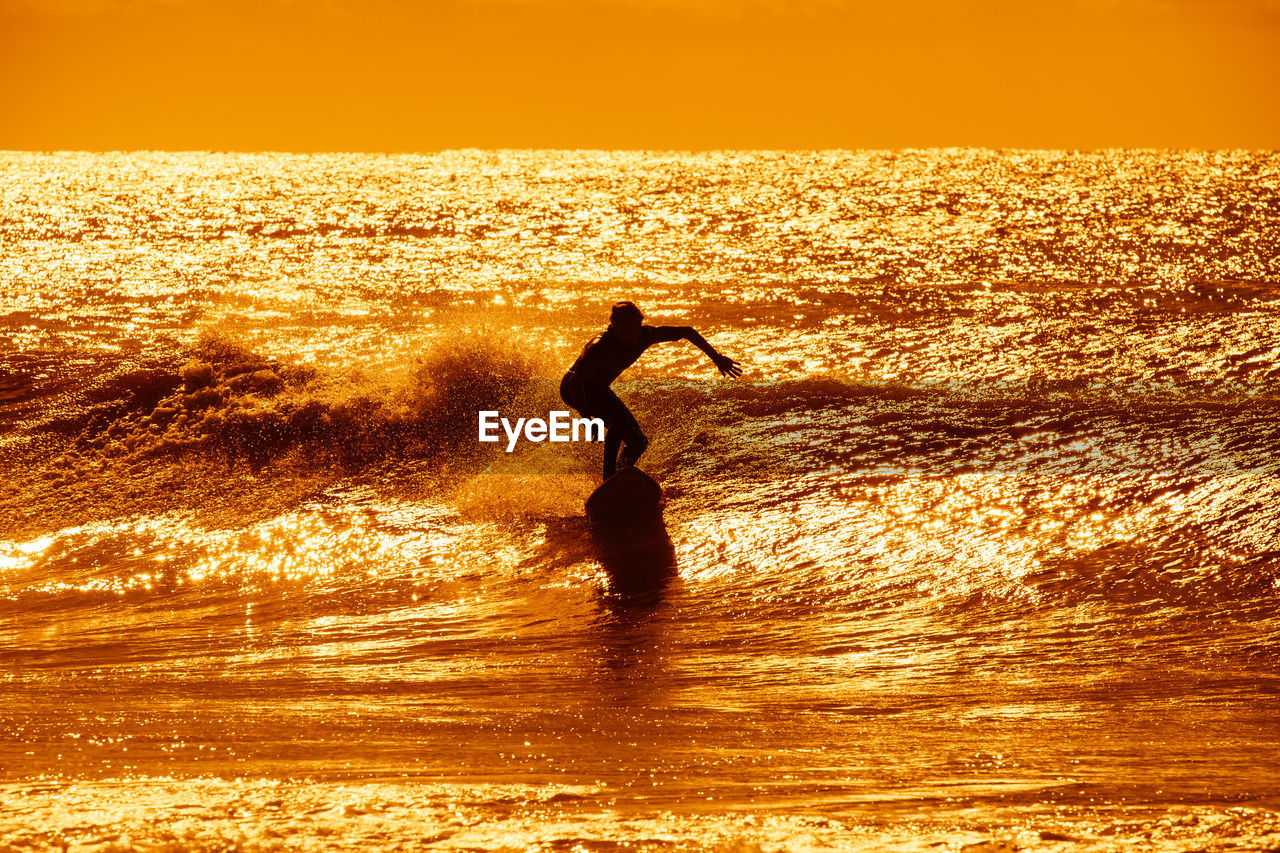 SILHOUETTE MAN ON BEACH AGAINST ORANGE SKY