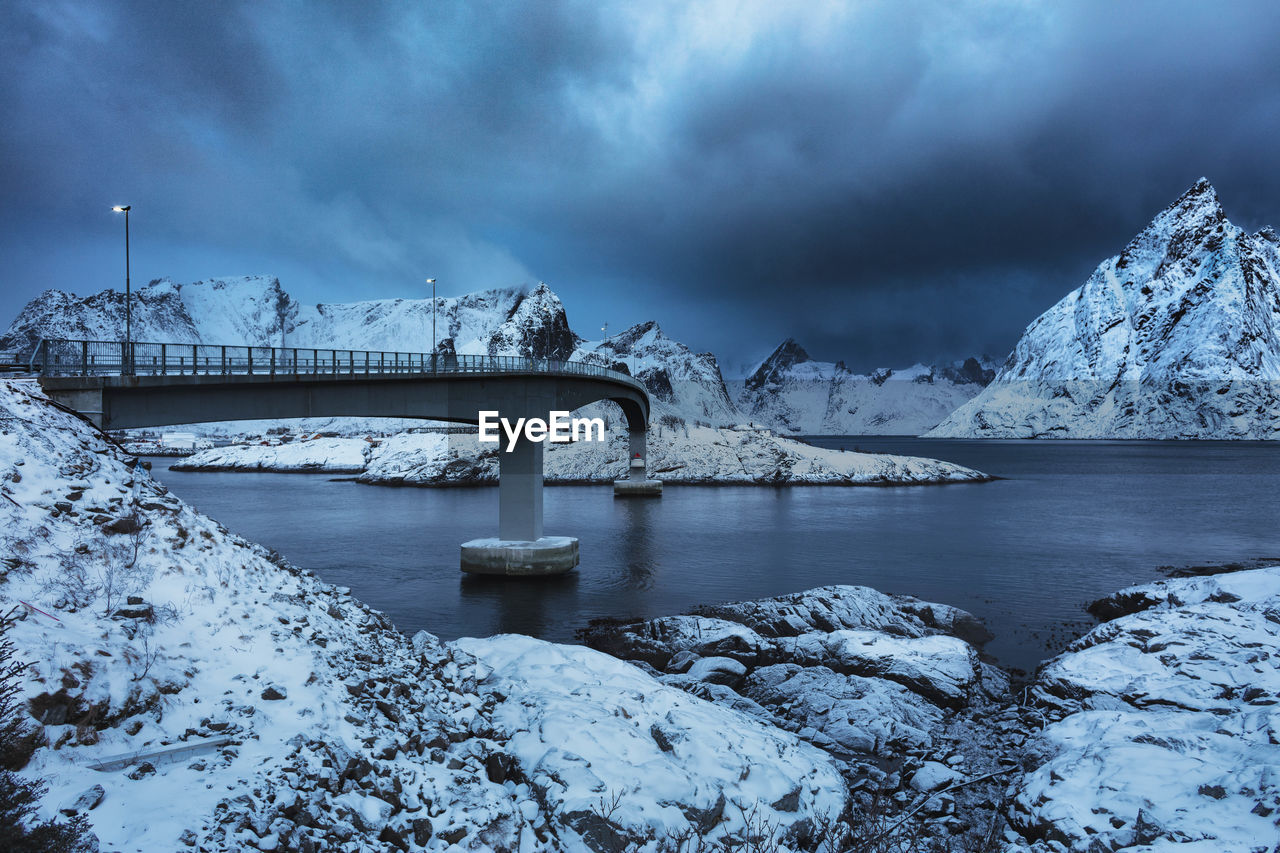 Bridge over lake amidst snowcapped mountains against cloudy sky during winter